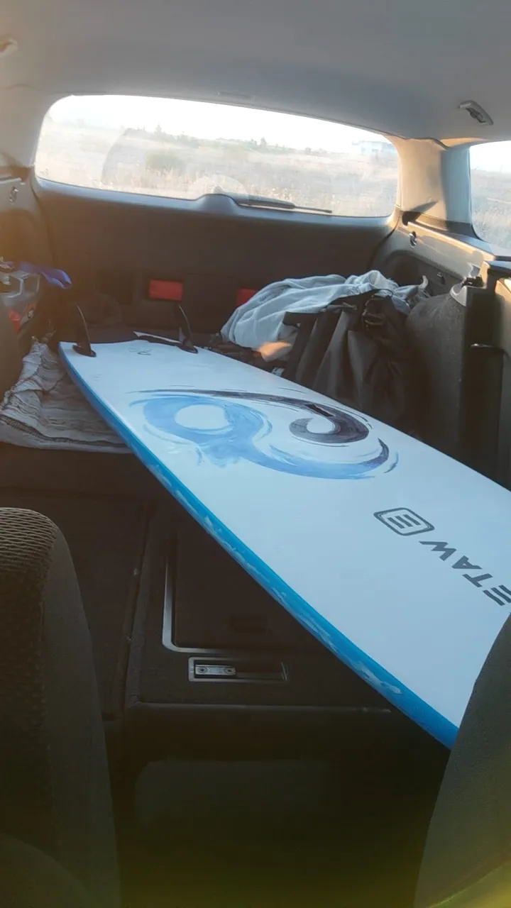 A white and blue soft-top surfboard laid diagonally across the folded-down back seats of a car.